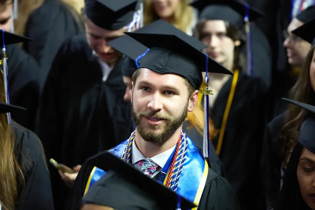 A U N E graduate student standing in the crowd of students waiting to cross the stage at commemcement 