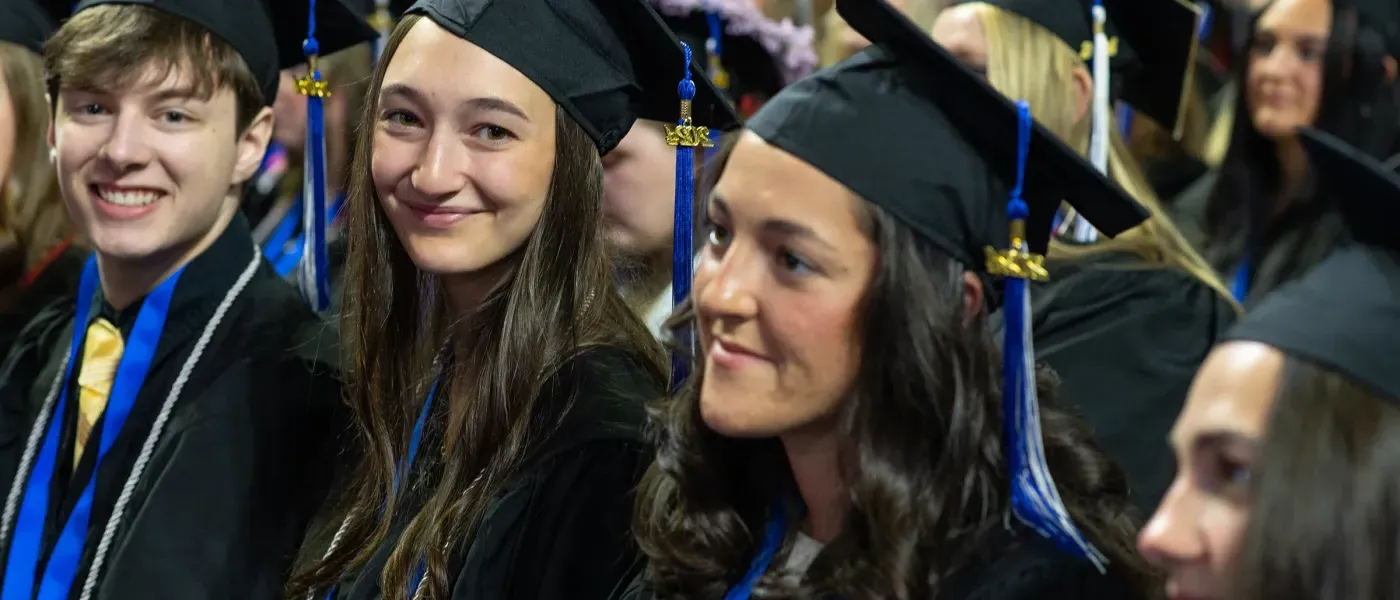 Two U N E graduate students look at the camera in a the crown of graduates before they listen to commencement speaker Bernie Sanders