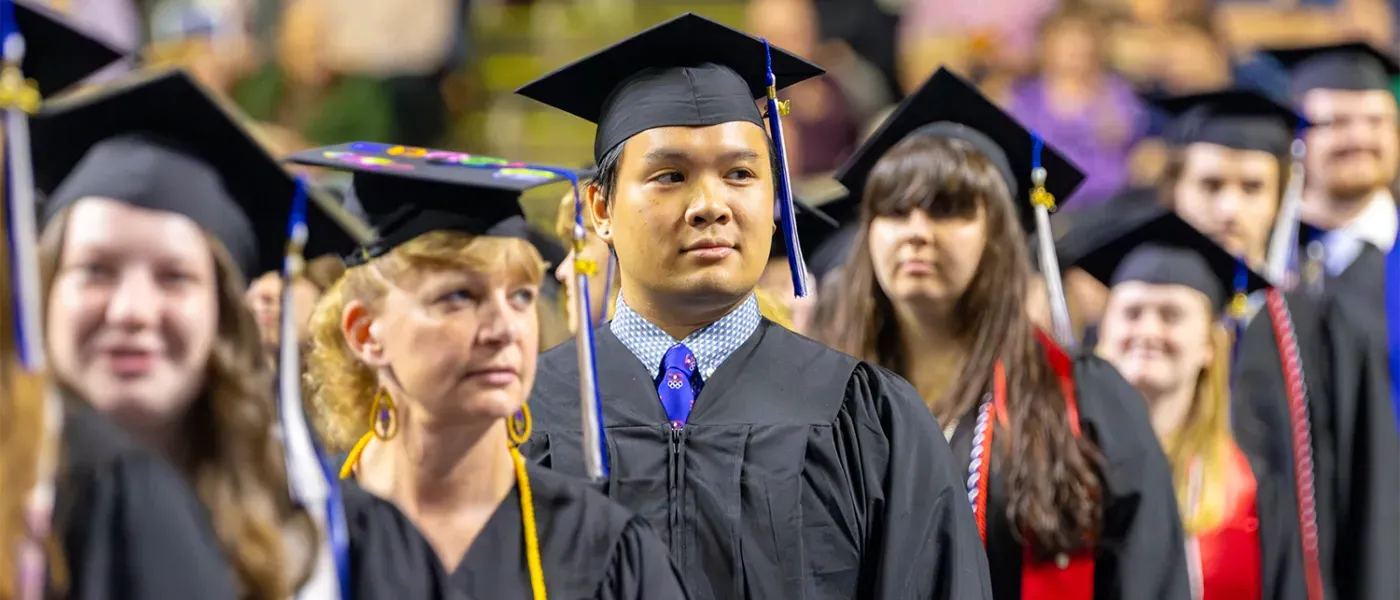 Undergraduate U N E students stand at 2024 commencement before crossing the stage